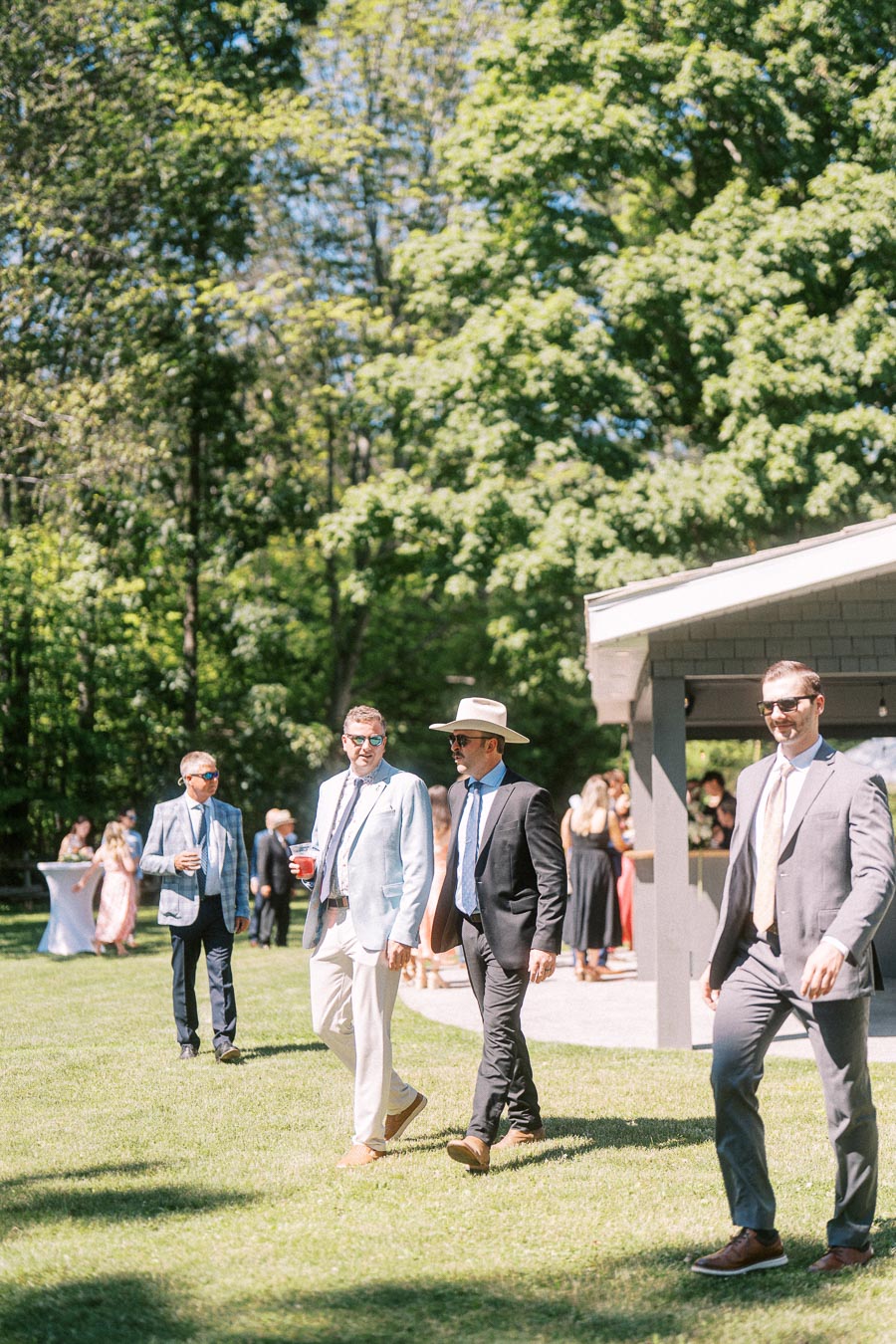 Wedding guests in suits walking on a sunny lawn during cocktail hour at a private estate near Chatham-Kent, Ontario, Canada.