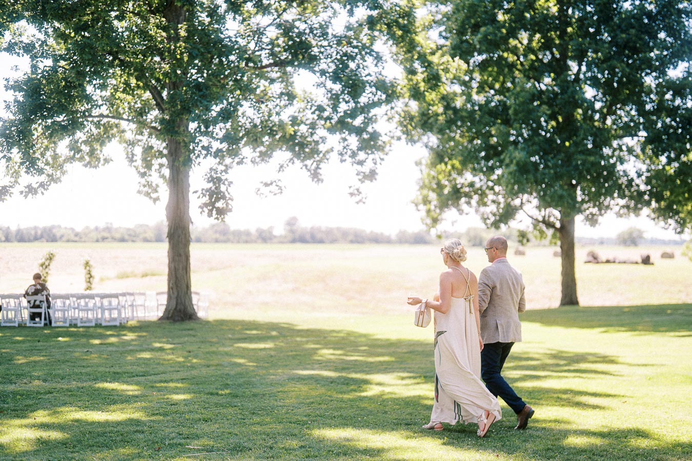 Guests walking across a shaded lawn toward white chairs set for an outdoor wedding ceremony on a private estate near Chatham-Kent, Ontario.