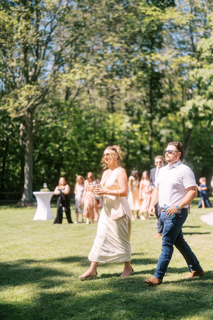 Wedding guests walking across a sunny lawn during an outdoor private estate wedding near Chatham-Kent, Ontario, Canada.