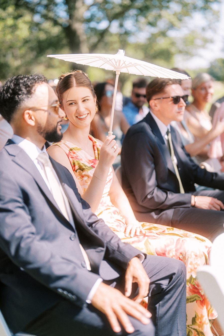 Wedding guests seated outdoors at a private estate ceremony near Chatham-Kent, Ontario, with a smiling woman holding a white parasol.