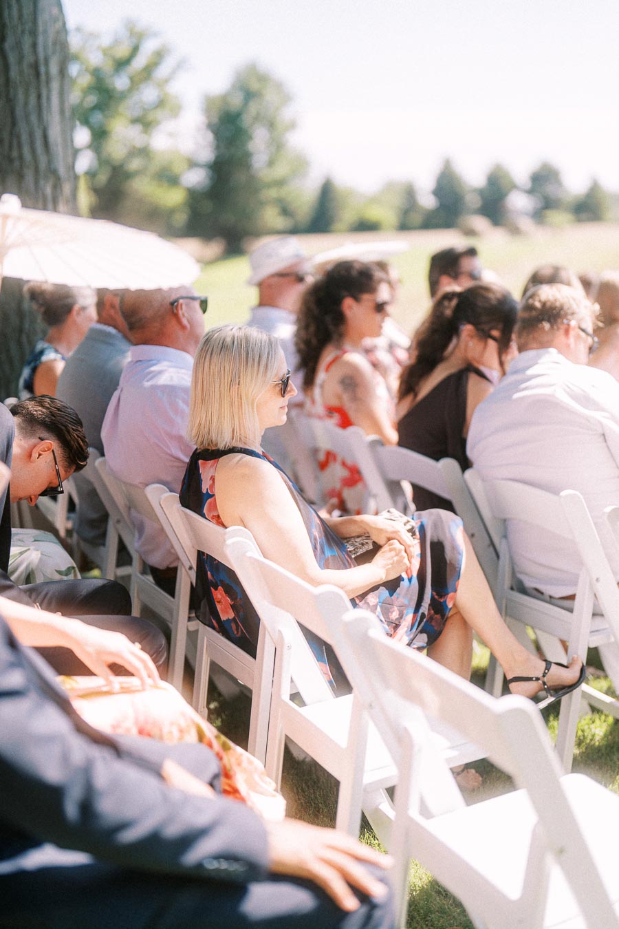 Wedding guests seated on white folding chairs during an outdoor ceremony on a private estate near Chatham-Kent, Ontario, Canada.