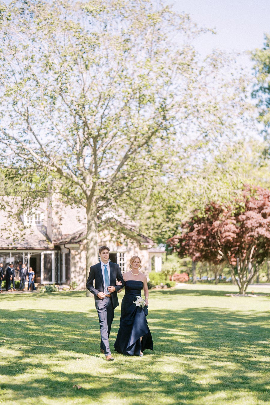 A man in a suit escorts a woman in a dark formal dress across a lawn during an outdoor private estate wedding near Chatham-Kent, Ontario.