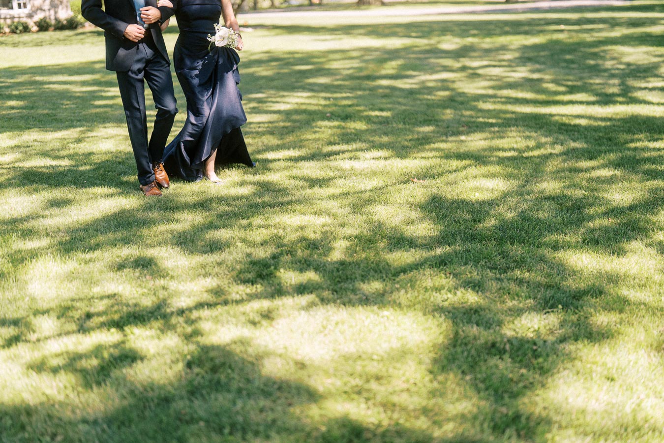 Wedding couple walking arm in arm across a sunlit lawn at a private outdoor estate near Chatham-Kent, Ontario, Canada.