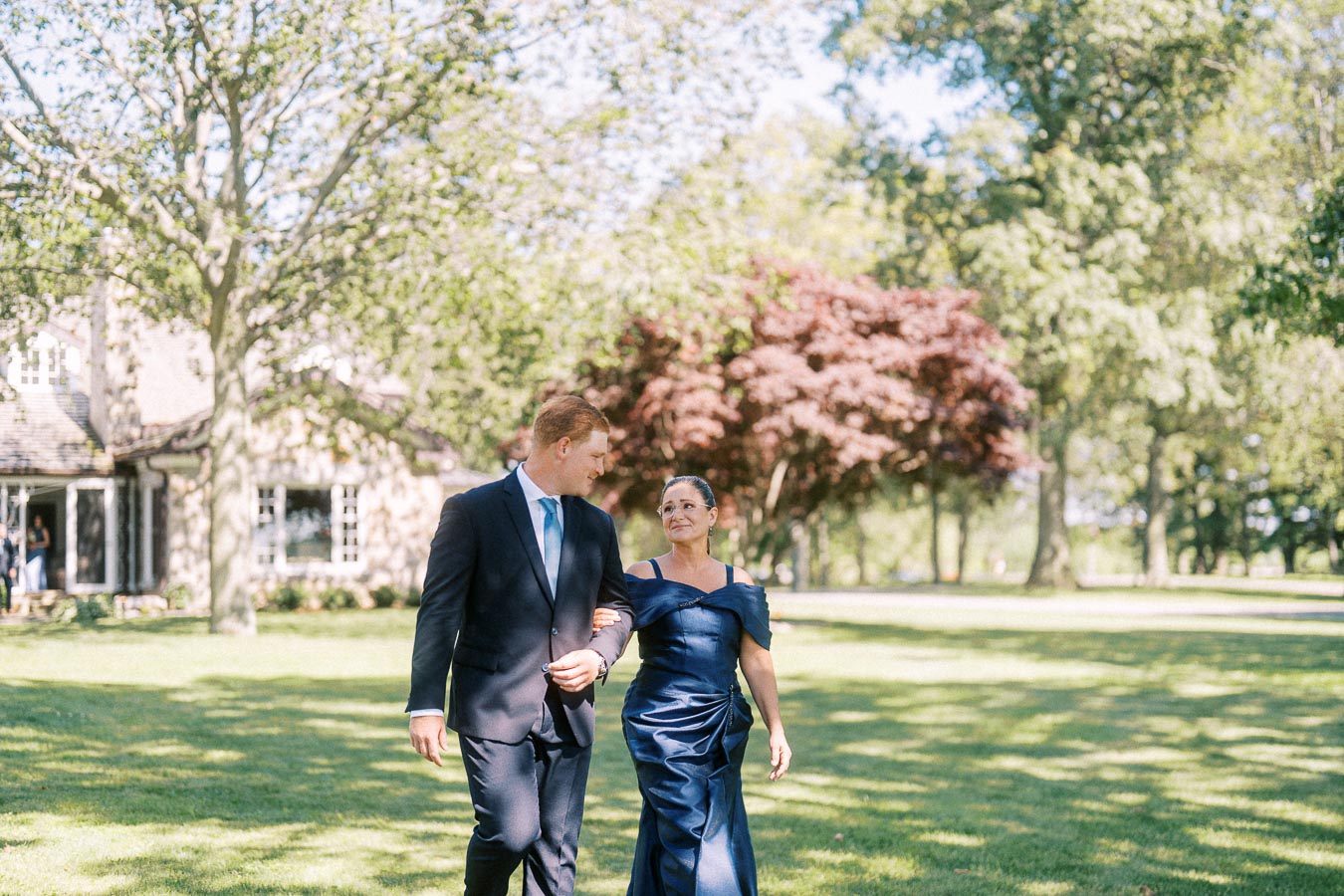 Well dressed man and woman walking arm in arm across a sunny lawn at a private estate wedding near Chatham-Kent, Ontario.