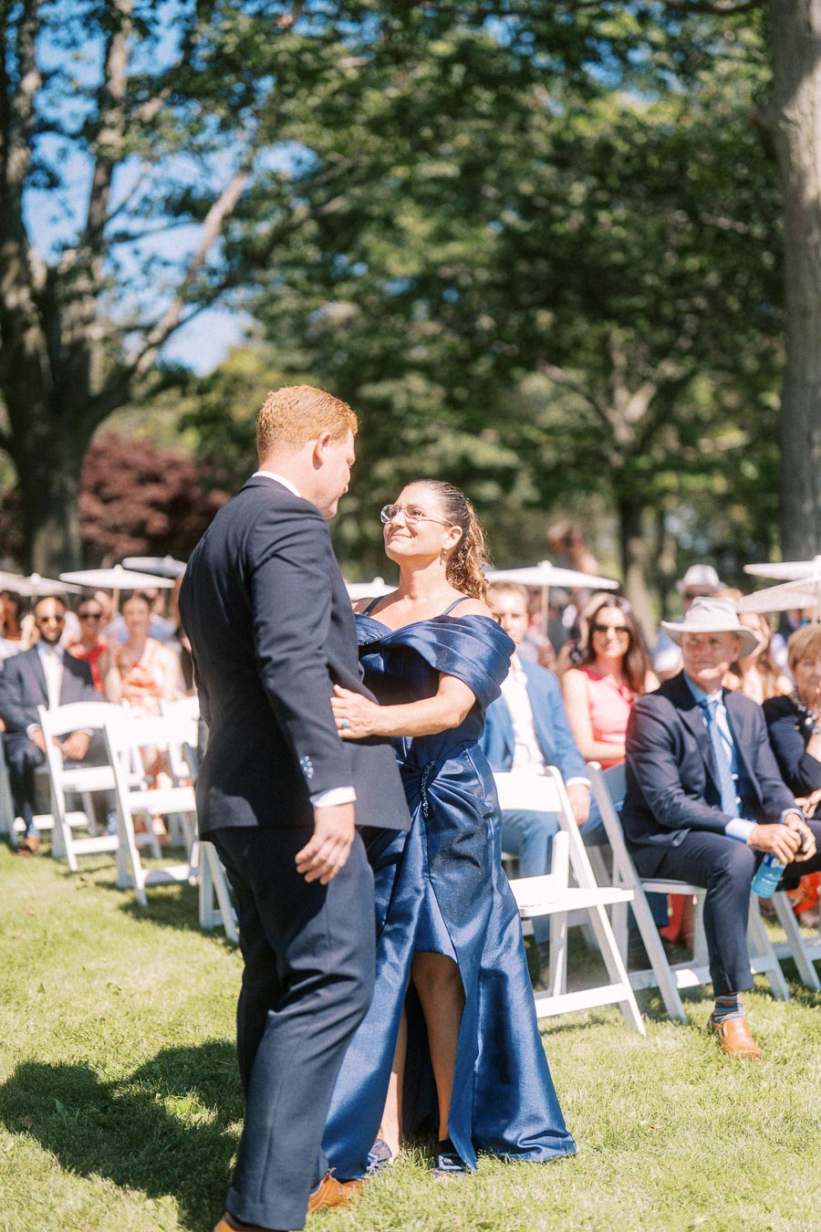 Groom embraces woman in blue dress during an outdoor wedding ceremony with seated guests on a private estate near Chatham-Kent, Ontario.
