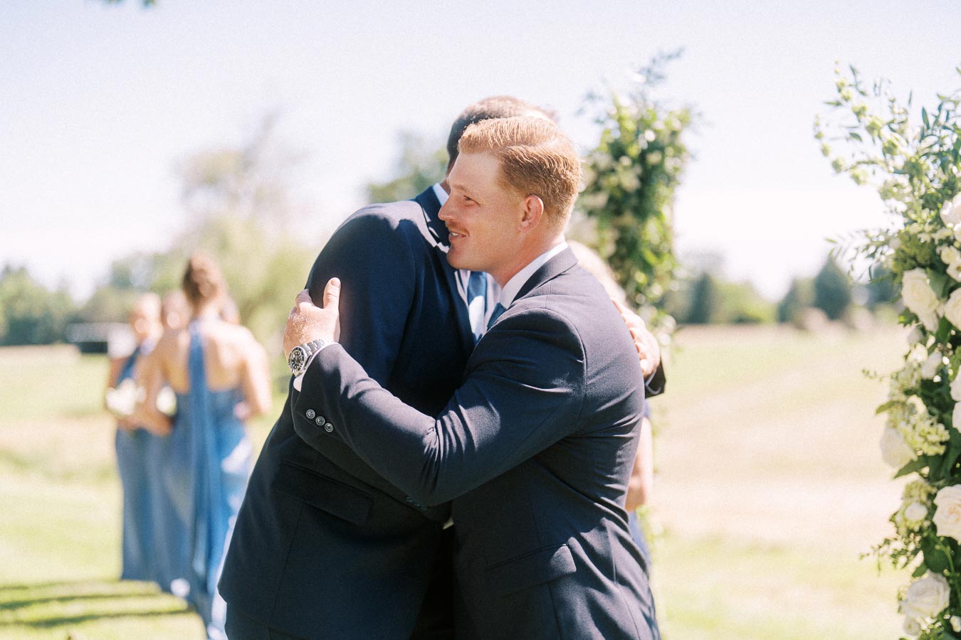 Groom in a navy suit hugging a wedding guest during an outdoor private estate wedding ceremony near Chatham-Kent, Ontario, Canada.
