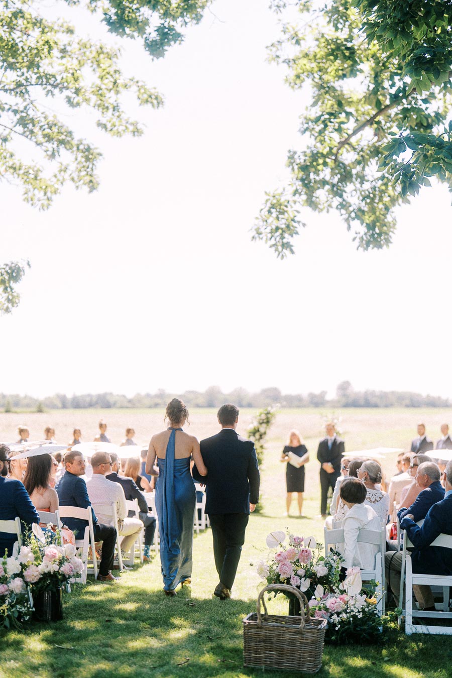 Couple walking down a grassy aisle at an outdoor private estate wedding ceremony near Chatham-Kent, Ontario, with seated guests and floral arrangements.