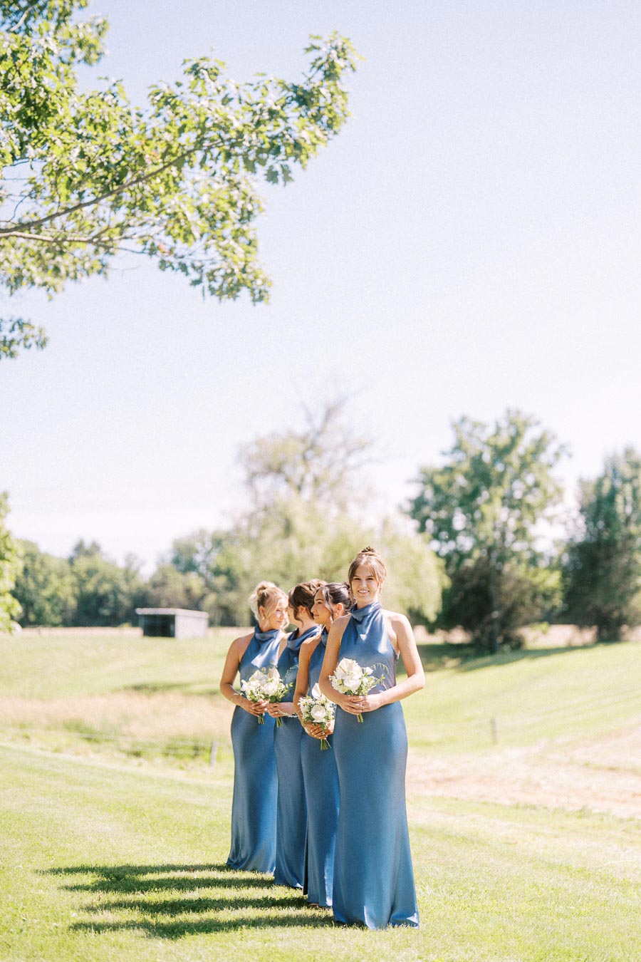 Bridesmaids in blue dresses holding white bouquets on a sunny private estate lawn near Chatham-Kent, Ontario.