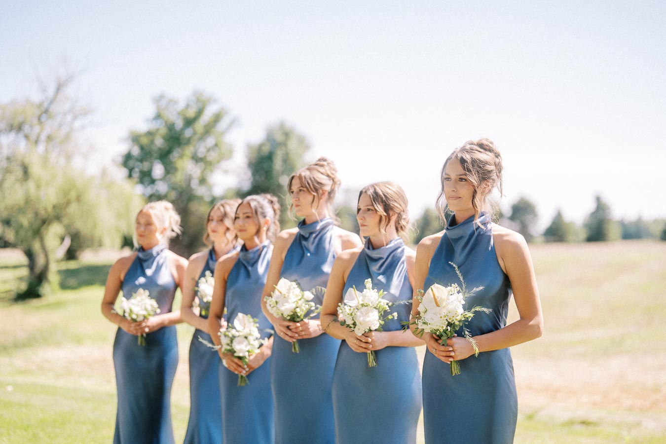 Bridesmaids in blue dresses holding white bouquets during an outdoor private estate wedding near Chatham-Kent, Ontario, Canada.