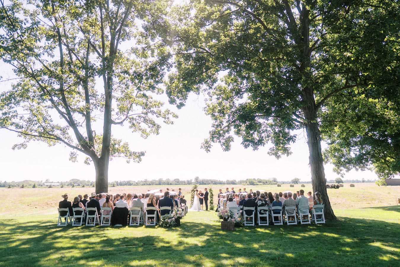 Outdoor private estate wedding ceremony under large trees beside farmland near Chatham-Kent, Ontario, Canada.
