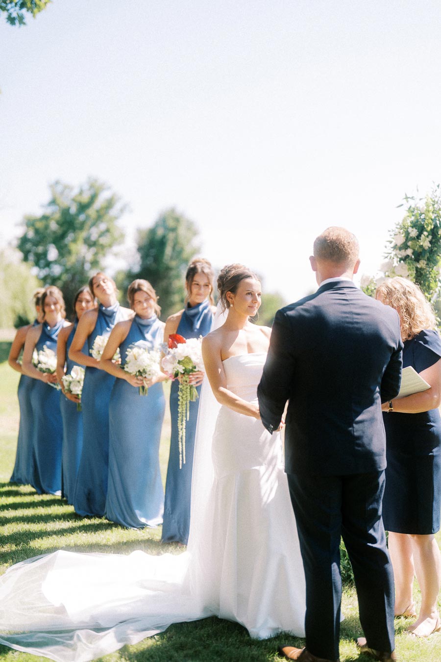Bride and groom exchange vows during an outdoor private estate wedding ceremony near Chatham-Kent, Ontario, with bridesmaids in blue dresses holding bouquets.