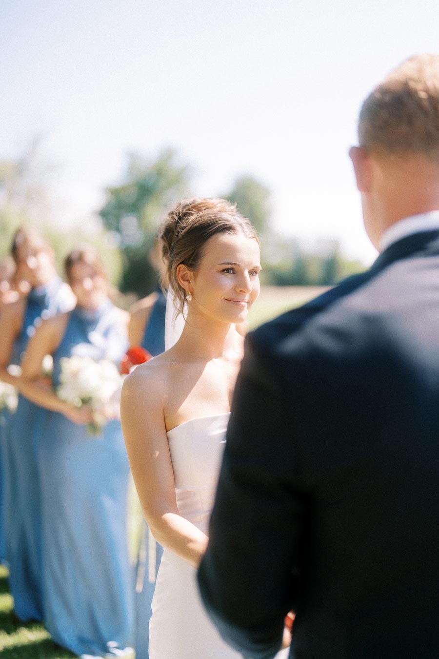 Bride facing groom during an outdoor wedding ceremony in Chatham-Kent, Ontario, with bridesmaids in blue dresses behind her.
