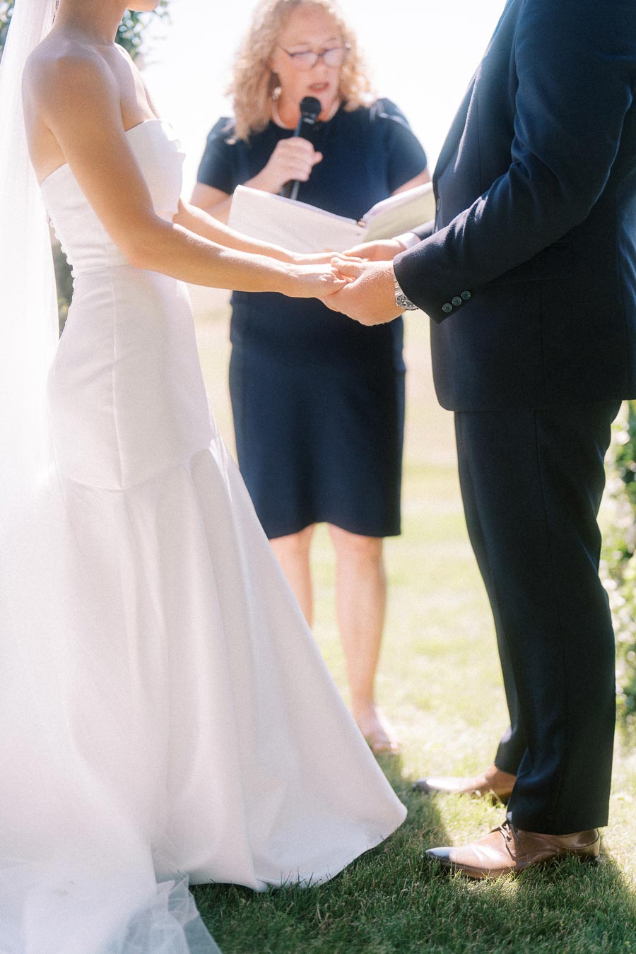 Bride and groom hold hands during an outdoor wedding ceremony with an officiant reading from a book near Chatham-Kent, Ontario, Canada.