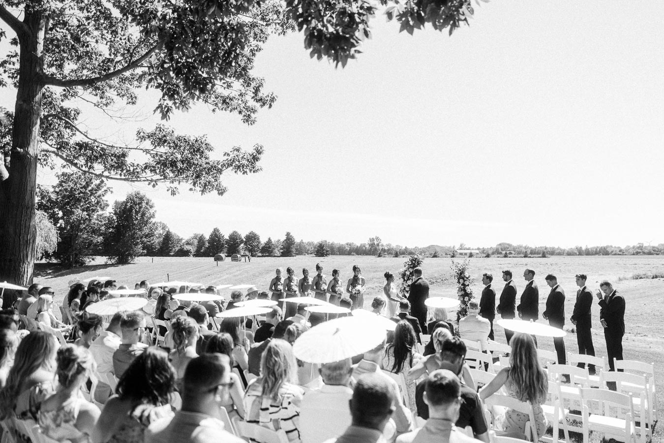 Black and white photo of an outdoor wedding ceremony on a private estate near Chatham-Kent, Ontario, with guests seated under trees.