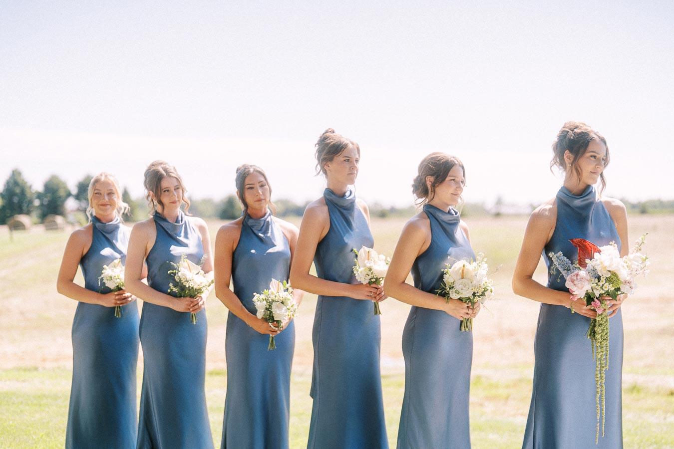 Six bridesmaids in blue dresses holding bouquets during an outdoor wedding on a rural property near Chatham-Kent, Ontario, Canada.
