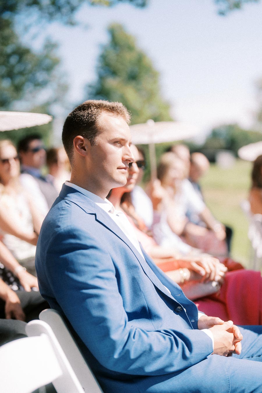 Man in blue suit seated among guests at an outdoor wedding ceremony near Chatham-Kent, Ontario, Canada.