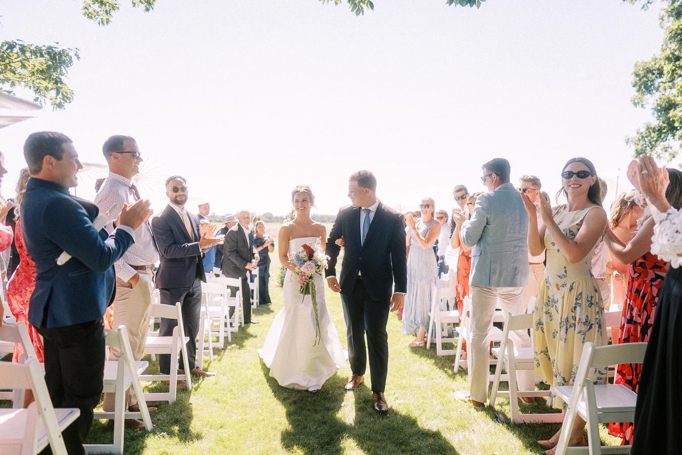 Bride and groom walk down a grassy aisle as guests applaud during an outdoor wedding ceremony near Chatham-Kent, Ontario.