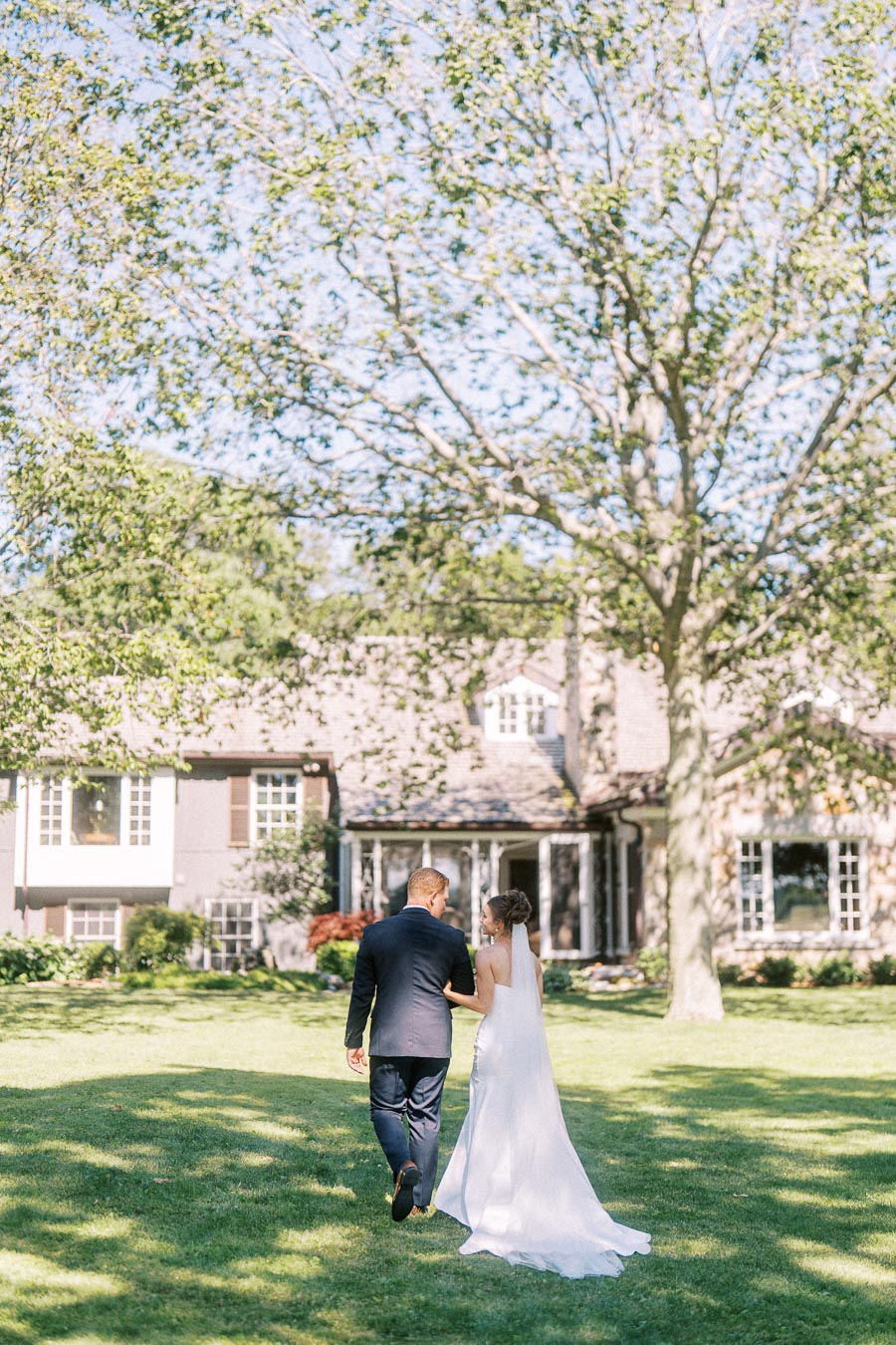 Bride and groom walking across a green lawn toward a private estate house in Chatham-Kent, Ontario, during an outdoor wedding.