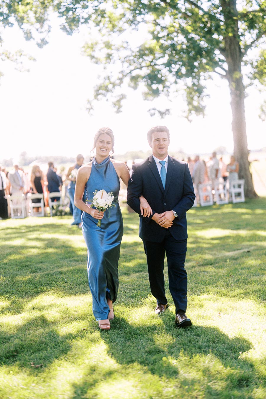 Wedding attendants walking arm in arm down a grassy outdoor aisle during a private estate ceremony in Chatham-Kent, Ontario.