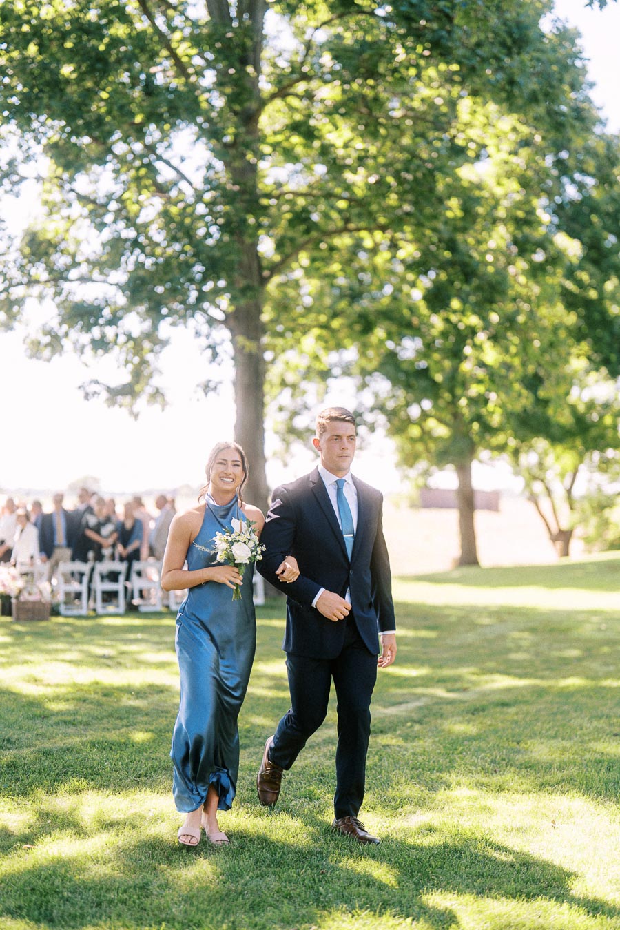 Wedding guests walking arm in arm on a sunny lawn at an outdoor private estate ceremony near Chatham-Kent, Ontario, Canada.