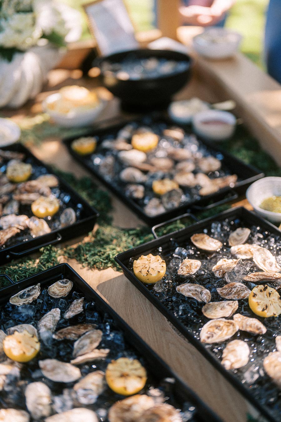 Oyster bar with oysters on ice, grilled lemons, herbs, and sauces at an outdoor private estate wedding near Chatham-Kent, Ontario.