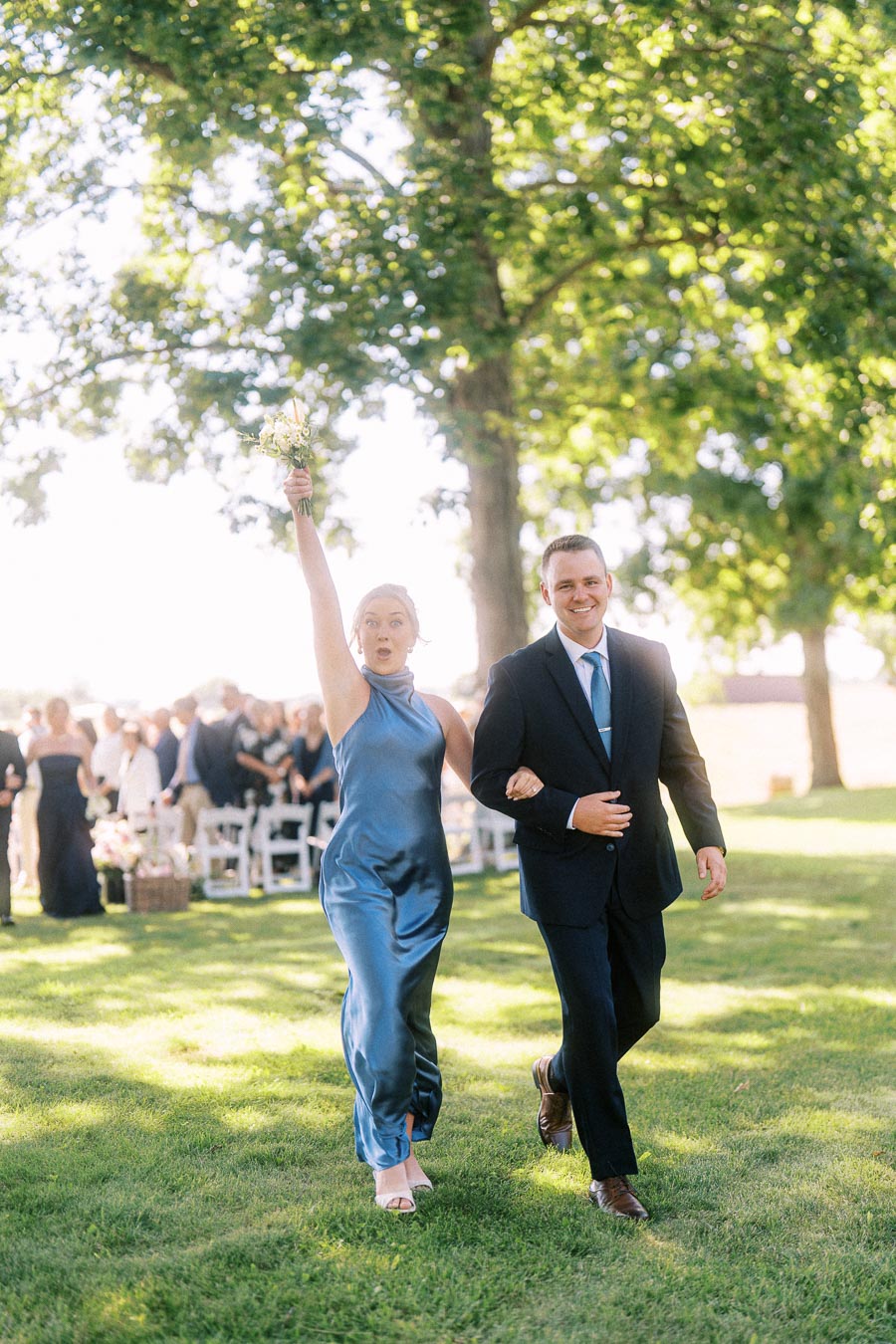 Wedding attendants walk down a grassy outdoor aisle at a private estate ceremony near Chatham-Kent, Ontario, with guests seated under trees.