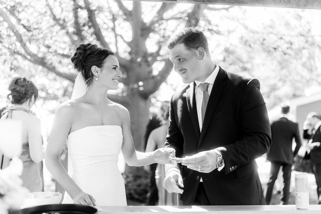 Black and white photo of a bride and groom smiling at an oyster bar during an outdoor wedding reception near Chatham-Kent, Ontario.