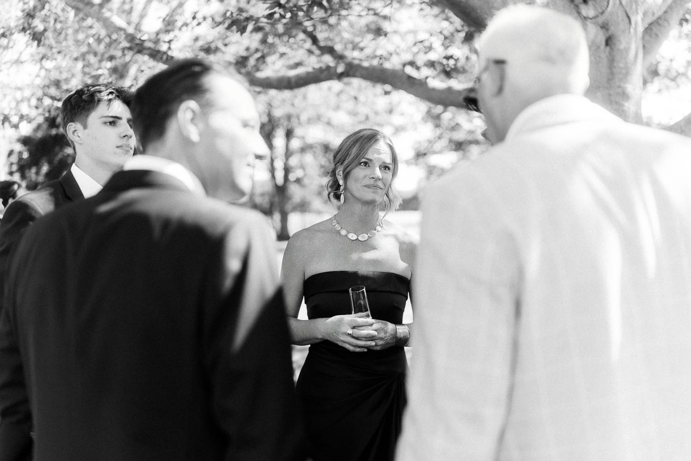 Black and white outdoor wedding guests talking under trees at a private farm estate near Chatham-Kent, Ontario, Canada.