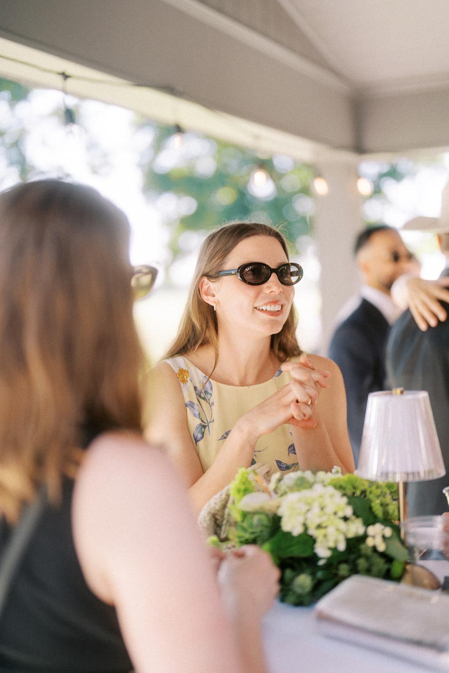 Guests talking at a tented outdoor wedding reception near Chatham-Kent, Ontario, with flowers and table lamp on a private estate.