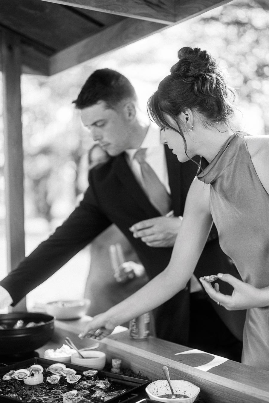 Black and white photo of wedding guests enjoying oysters at an outdoor tented farm wedding near Chatham-Kent, Ontario, Canada.