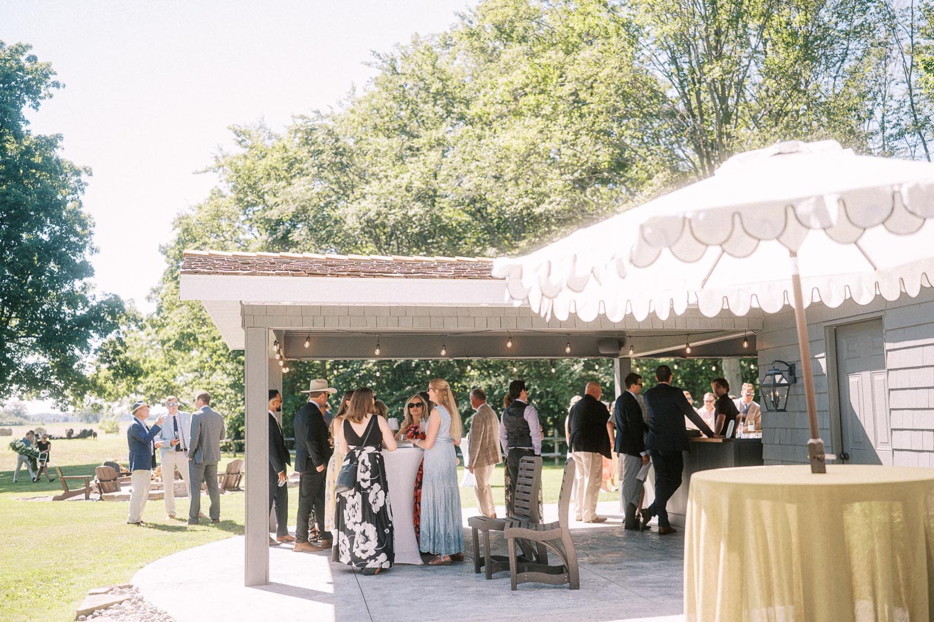 Wedding guests gather on a sunny private estate patio beside a white tent and farm lawn near Chatham-Kent, Ontario, Canada.