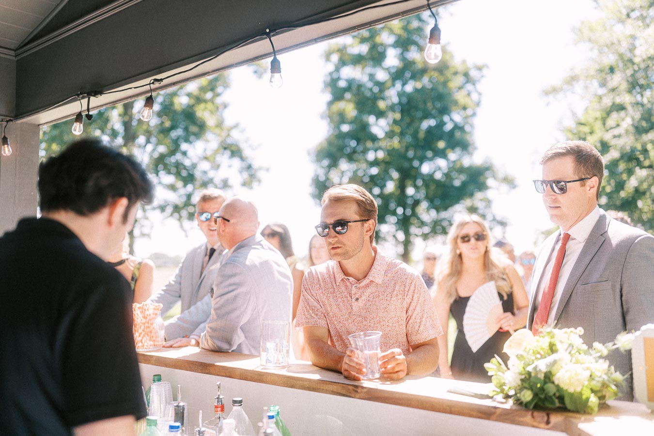 Wedding guests wearing sunglasses gather at an outdoor bar under a tent on a private estate near Chatham-Kent, Ontario.