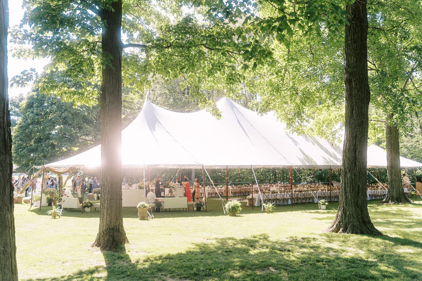White wedding reception tent with guests, tables, and chairs on a private estate lawn surrounded by mature trees near Chatham-Kent, Ontario, Canada.
