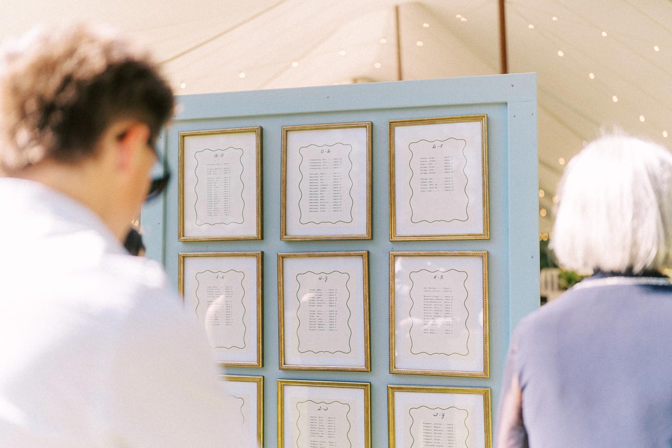 Wedding guests view a framed seating chart display outside a tented farm wedding near Chatham-Kent, Ontario, Canada.