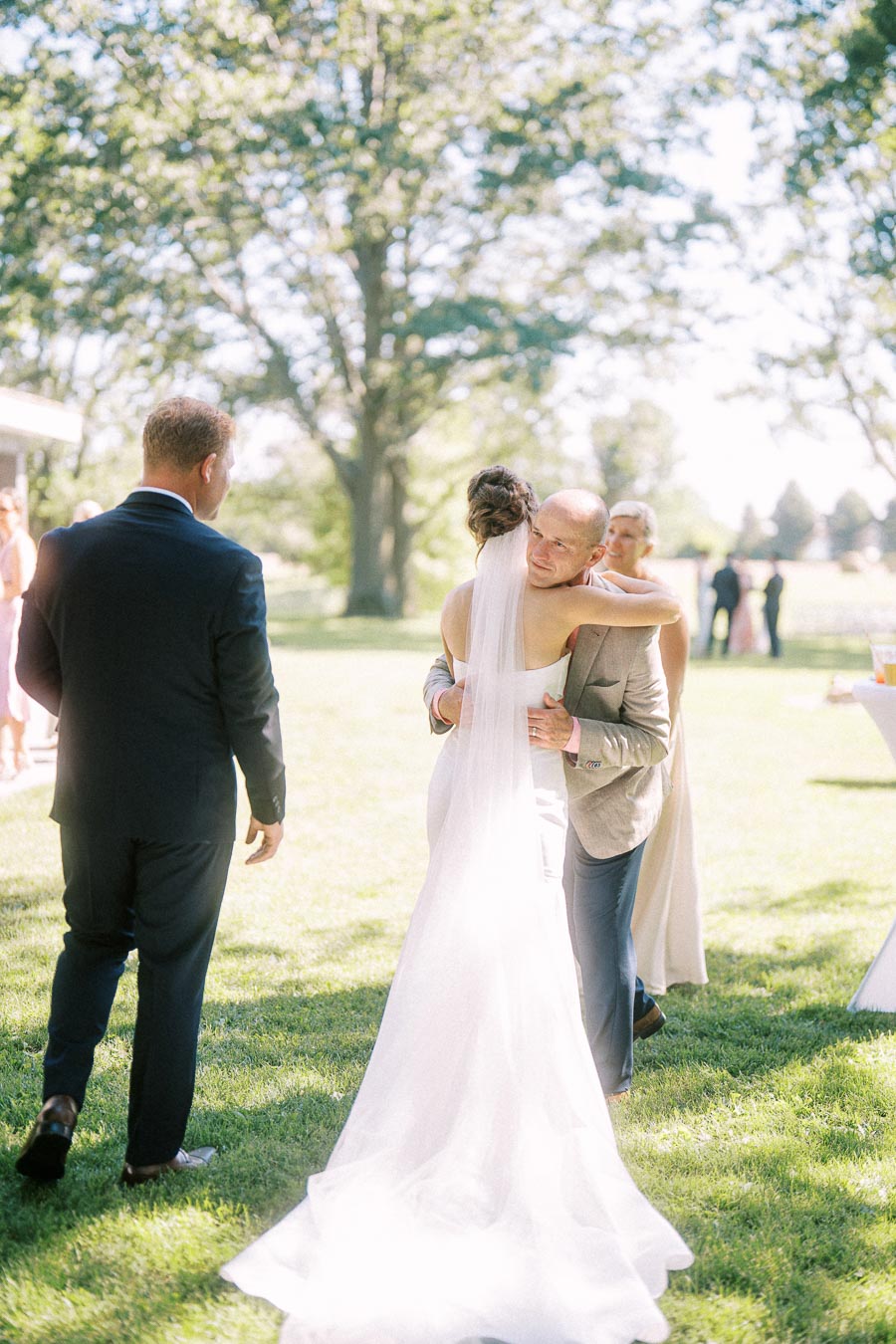 Bride in a white gown hugs a guest during an outdoor wedding reception on a grassy private estate near Chatham-Kent, Ontario.