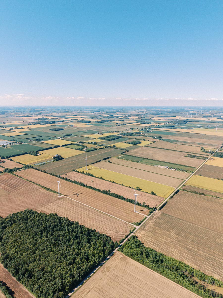Aerial view of farmland fields and wind turbines near Chatham-Kent, Ontario, Canada, under a clear blue sky.