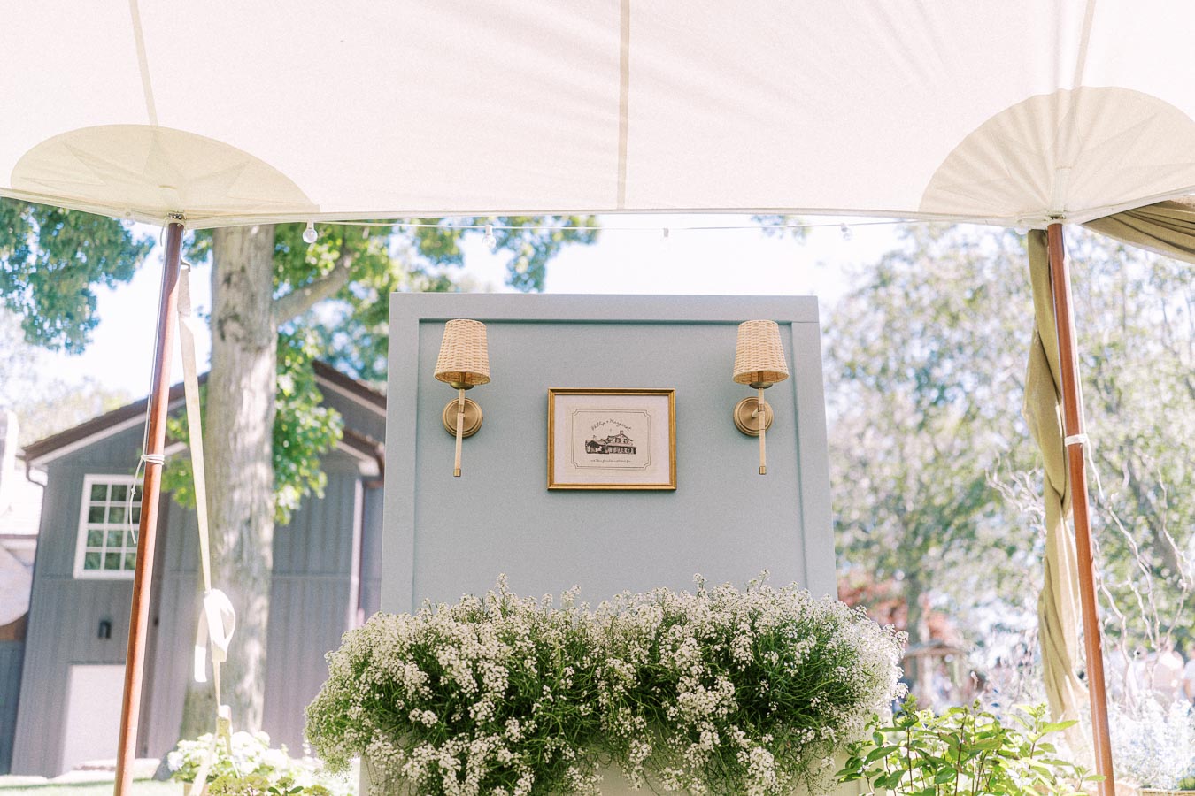 White floral wedding decor under a tent on a private farm estate near Chatham-Kent, Ontario, with wall sconces and a rustic building.