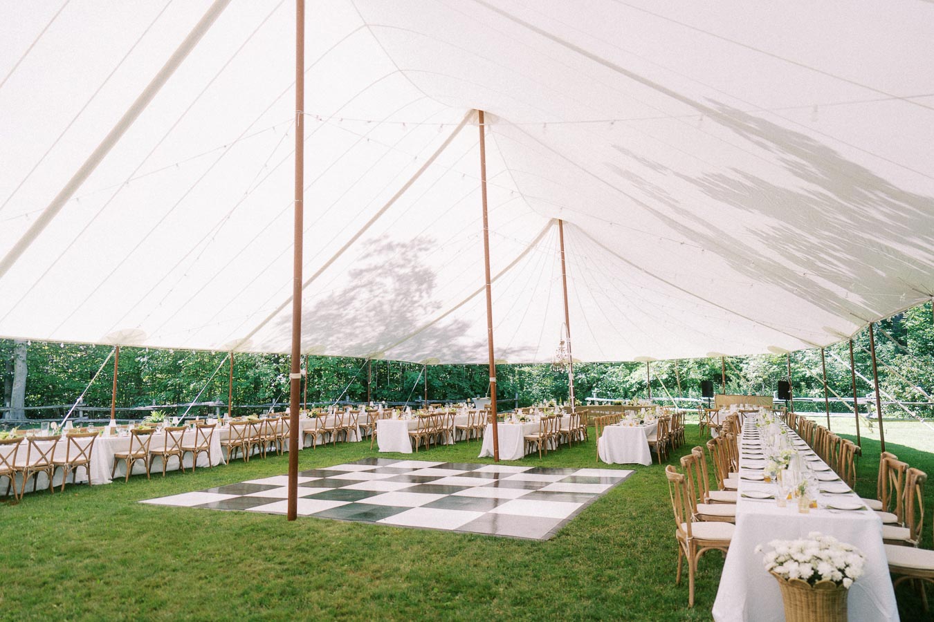 Outdoor tented wedding reception with long tables, wooden chairs, flowers, and a black and white dance floor on grass near Chatham-Kent, Ontario.
