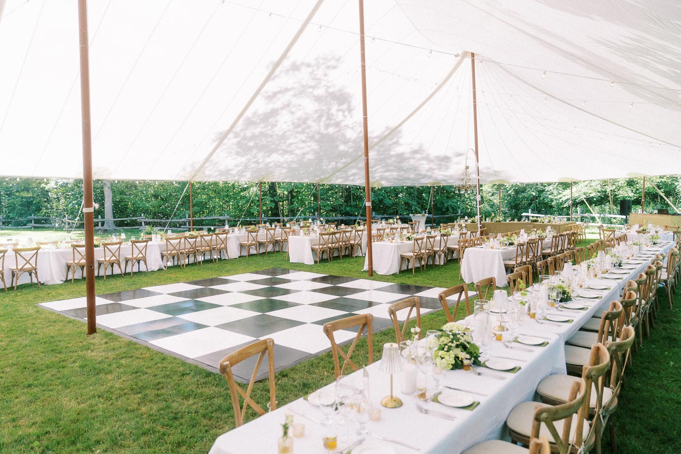 Outdoor tented wedding reception on a private farm estate near Chatham-Kent, Ontario, with long dining tables, wooden chairs, and a checkered dance floor.