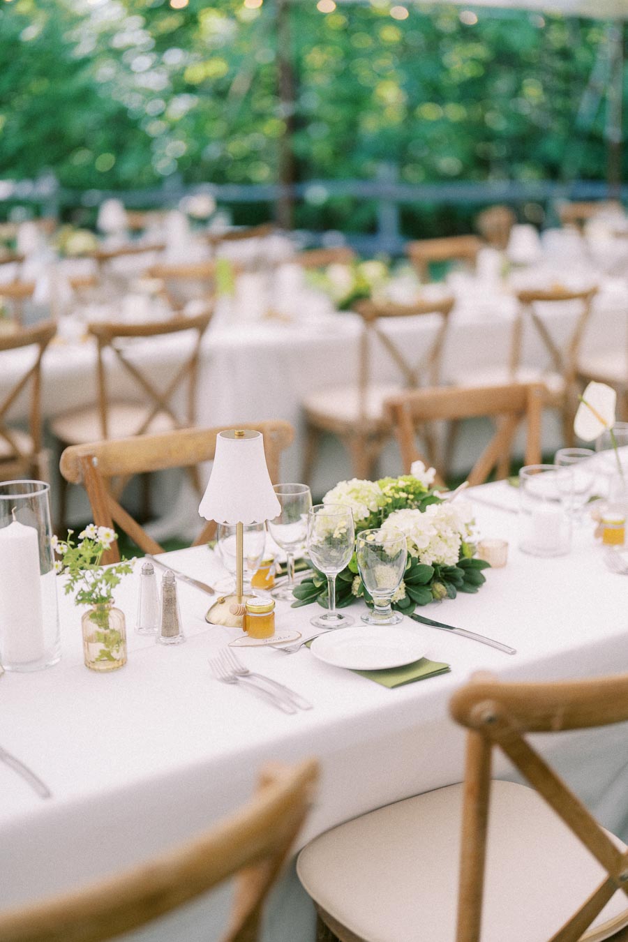 Outdoor tented wedding reception table with white linens, wooden chairs, floral centerpiece, glassware, candles, and small table lamp in Chatham-Kent, Ontario.