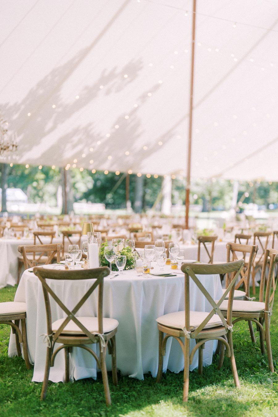 Outdoor tented wedding reception on a private farm estate near Chatham-Kent, Ontario, with round tables, white linens, wooden chairs, glassware, greenery, and string lights.