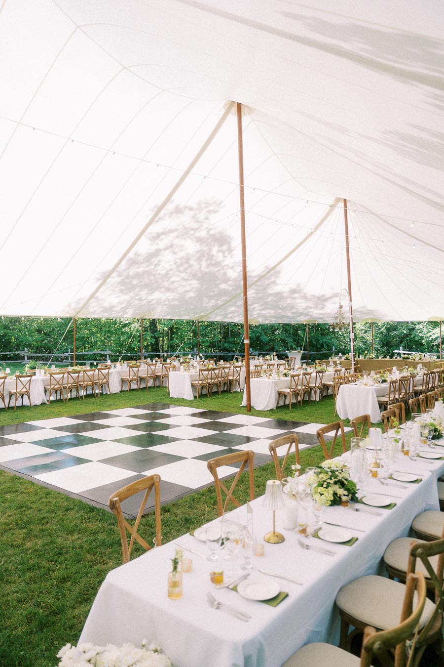 Outdoor tented wedding reception setup on a private farm estate near Chatham-Kent, Ontario, with long tables, wooden chairs, flowers, and a checkered dance floor.