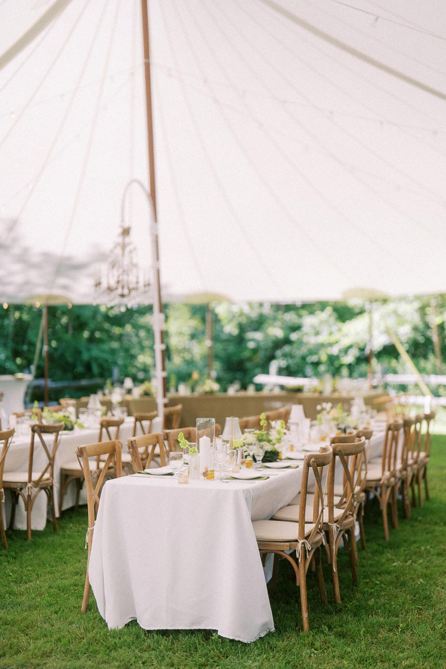 Outdoor tented farm wedding reception setup with long tables, white linens, wooden chairs, glassware, and greenery near Chatham-Kent, Ontario.