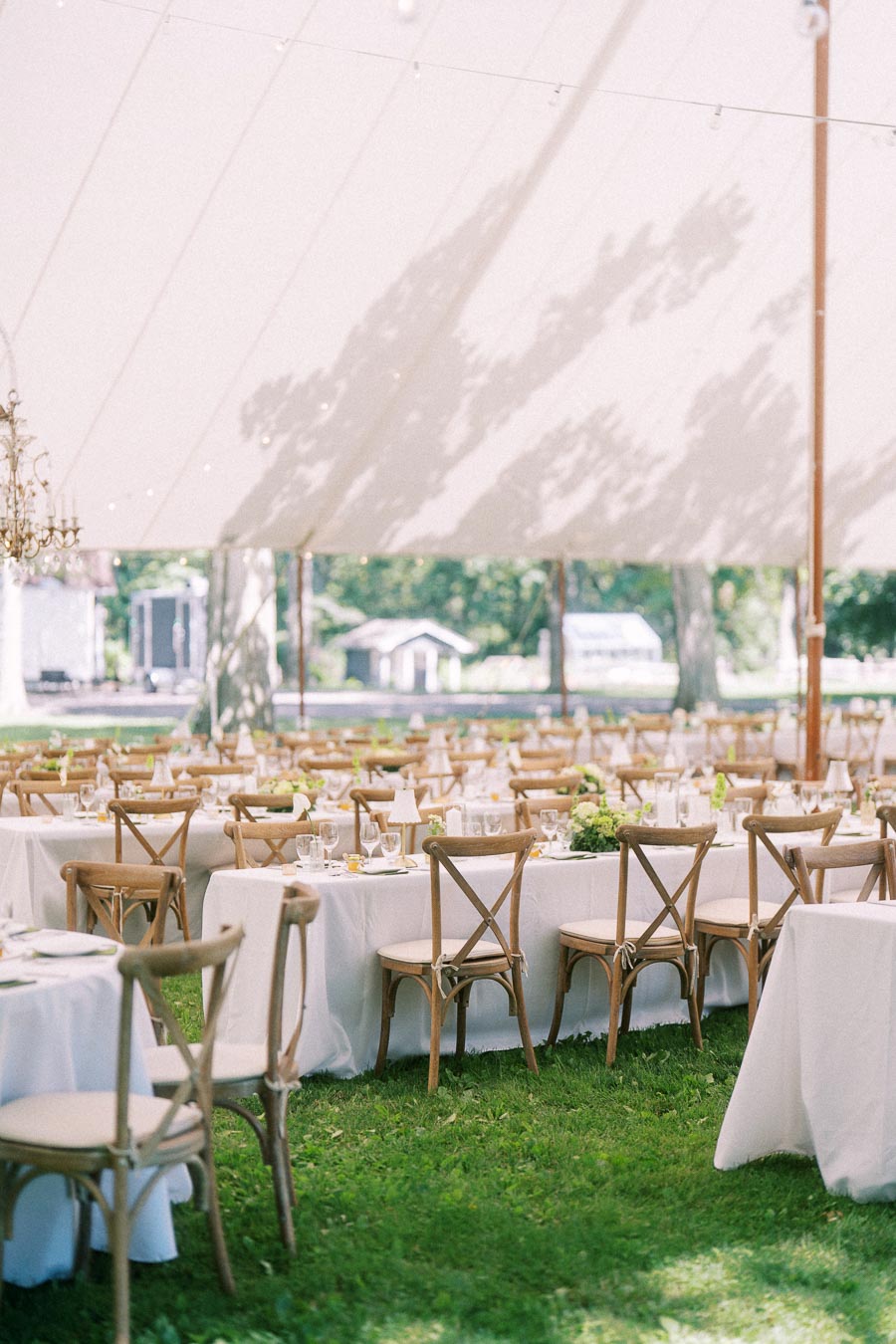 Outdoor tented wedding reception on a private farm estate near Chatham-Kent, Ontario, with round tables, wooden chairs, linens, glassware, and floral centerpieces.