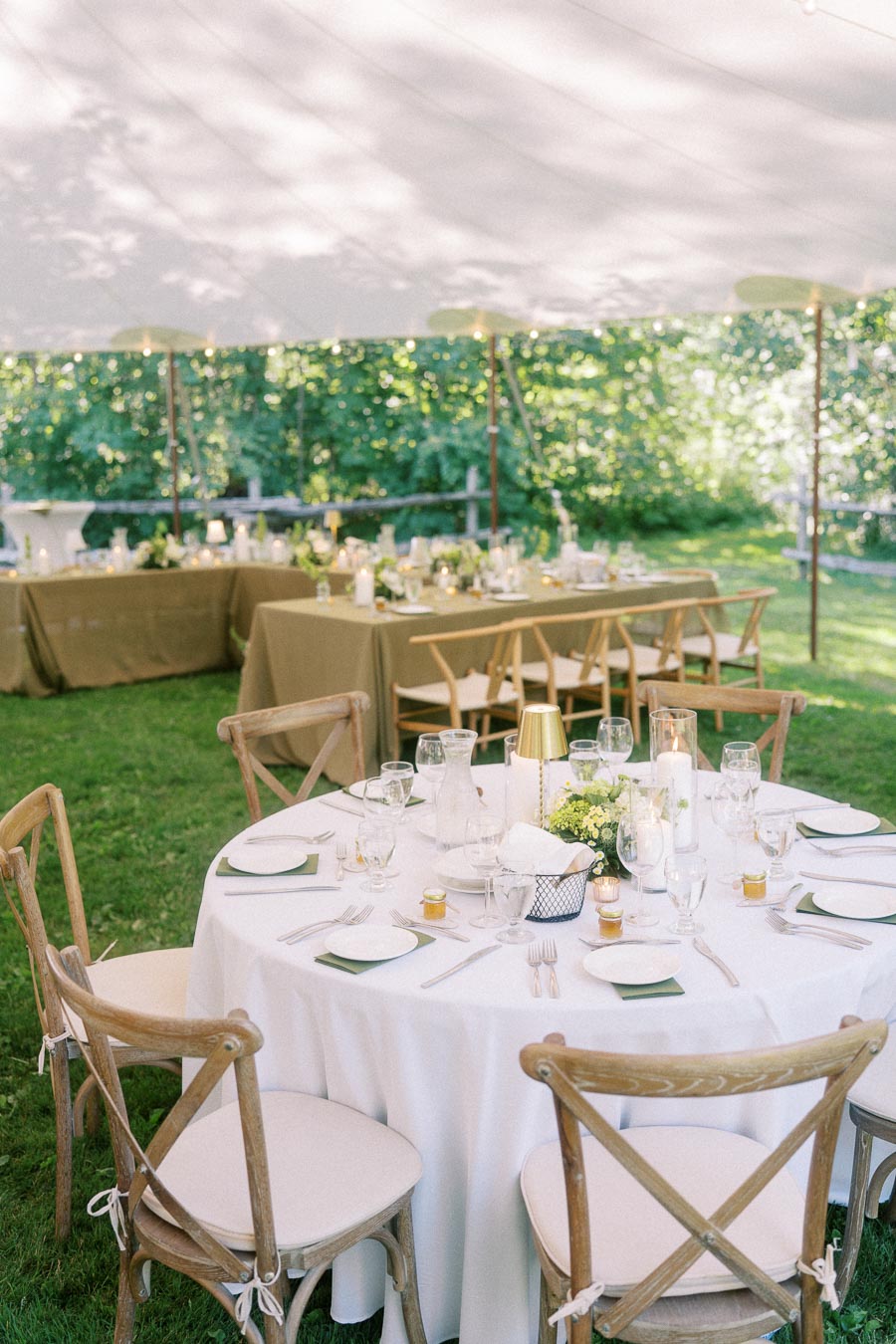 Outdoor tented wedding reception on a private farm estate near Chatham-Kent, Ontario, with round tables, wooden chairs, white linens, candles, and greenery.