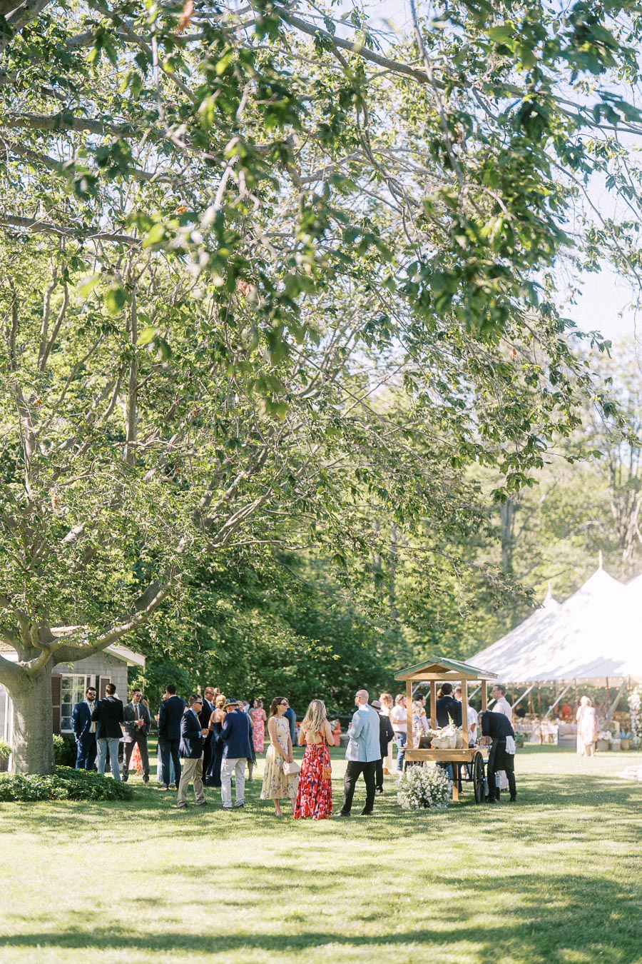 Wedding guests gather on a sunny lawn under trees beside a white reception tent on a private estate near Chatham-Kent, Ontario, Canada.