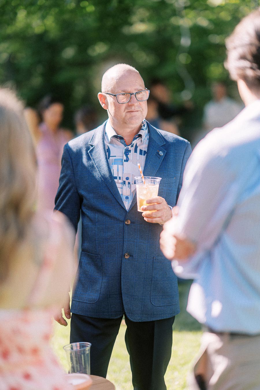 Man in a blue blazer holding a drink while talking with guests at an outdoor private estate wedding near Chatham-Kent, Ontario.