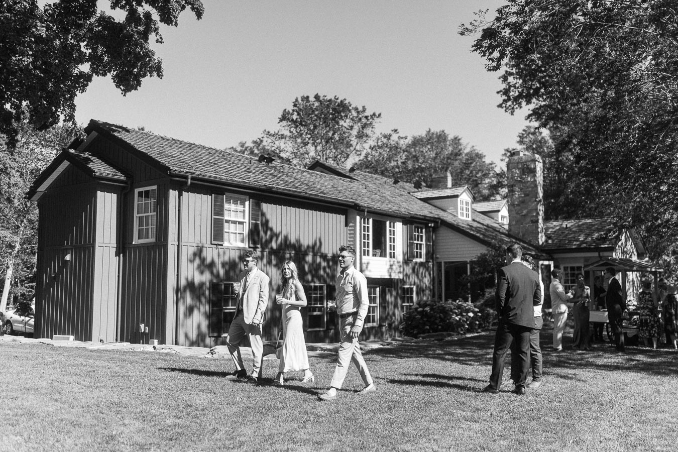 Black and white outdoor wedding guests walking on a lawn beside a private estate house near Chatham-Kent, Ontario, Canada.