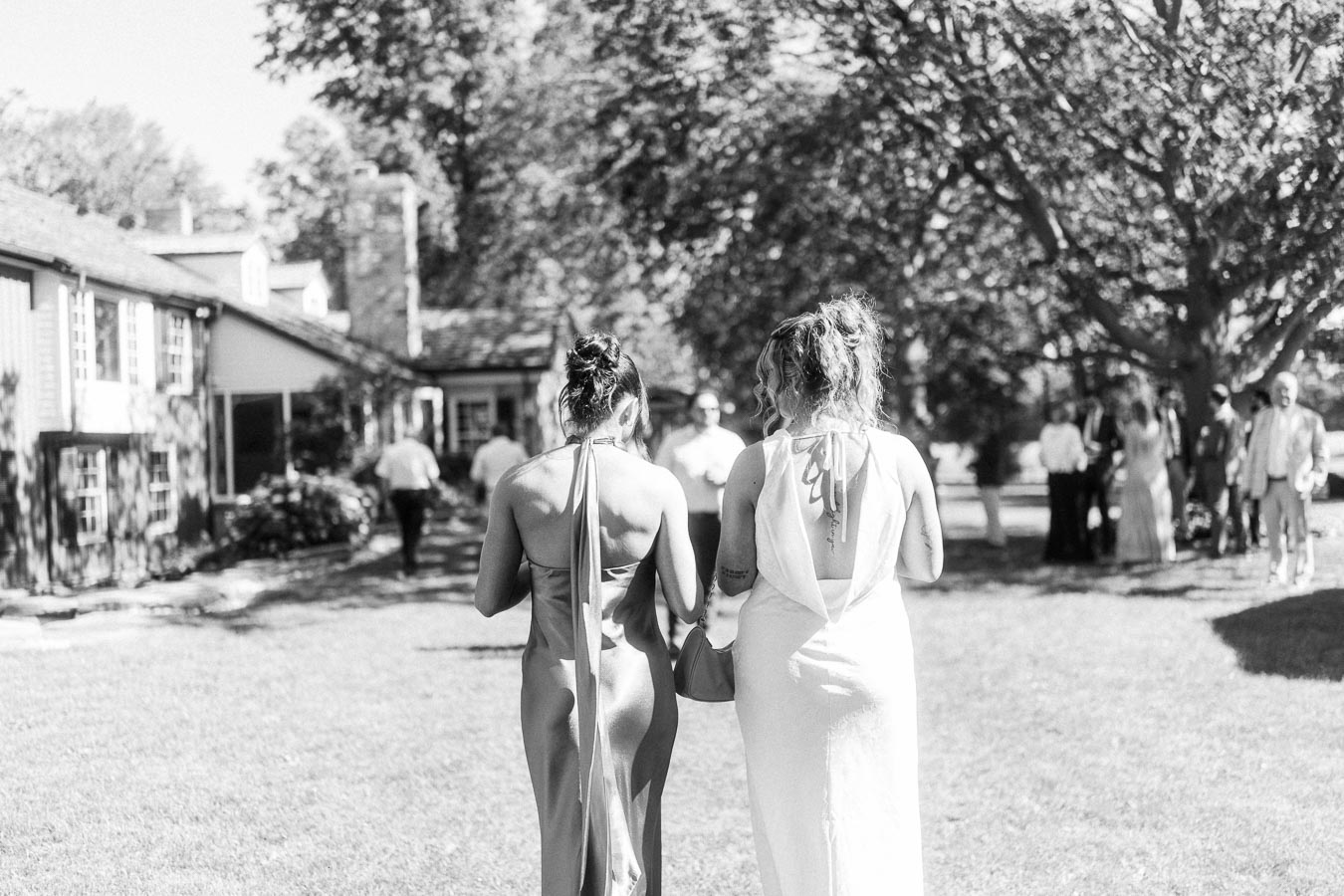 Black and white outdoor wedding scene on a private estate lawn near Chatham-Kent, Ontario, with two women walking toward guests by a farmhouse.