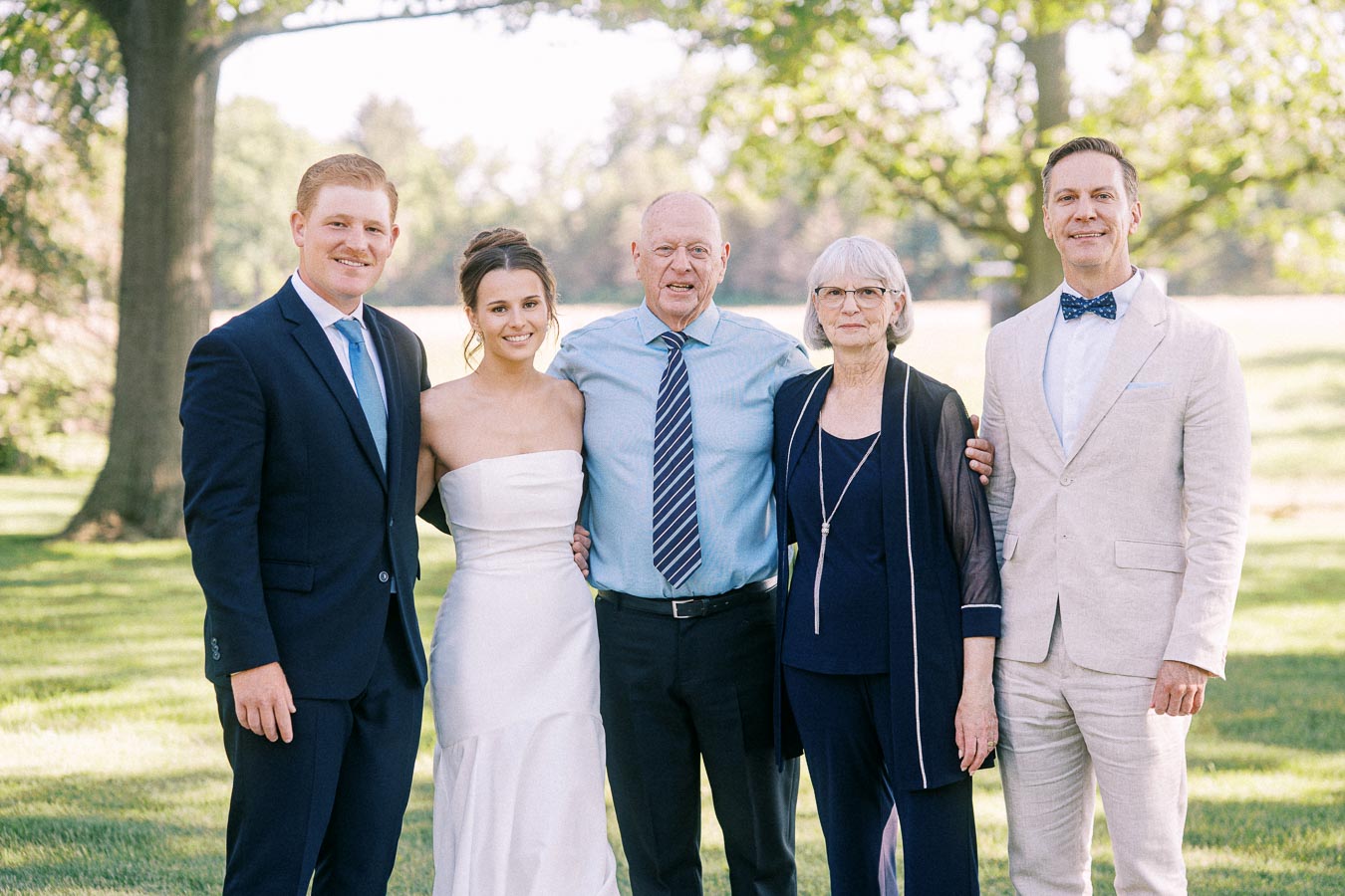 Wedding family portrait outdoors on a private estate lawn near Chatham-Kent, Ontario, with bride and relatives standing under trees.